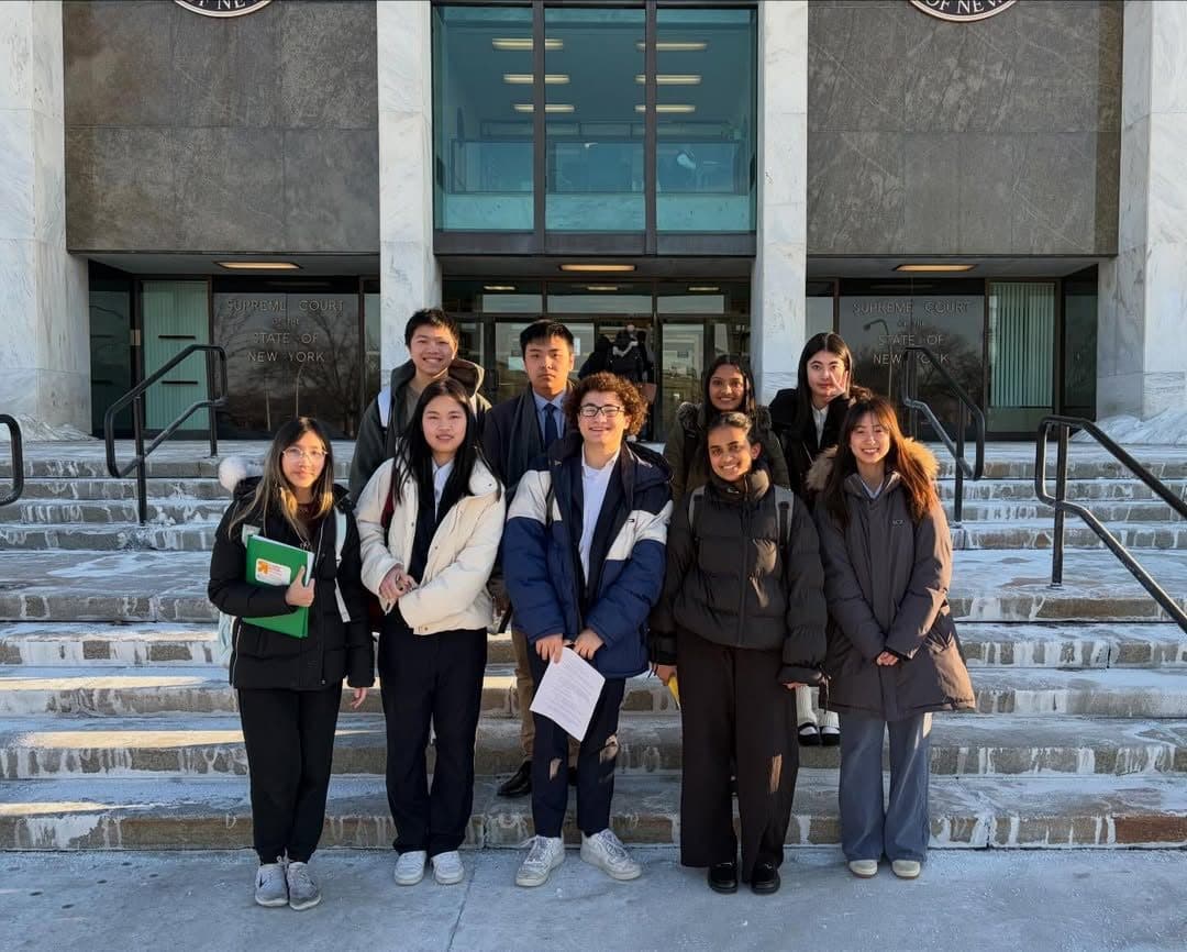 Nine students in coats standing on the stone steps of a courthouse in winter, with the words Supreme Court of the State of New York cut into the stone behind them.
