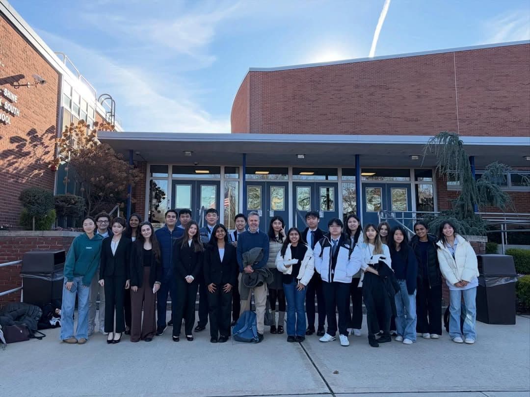 A wide line of about twenty-five students standing shoulder to shoulder outside a brick school entrance under a bright winter sky.